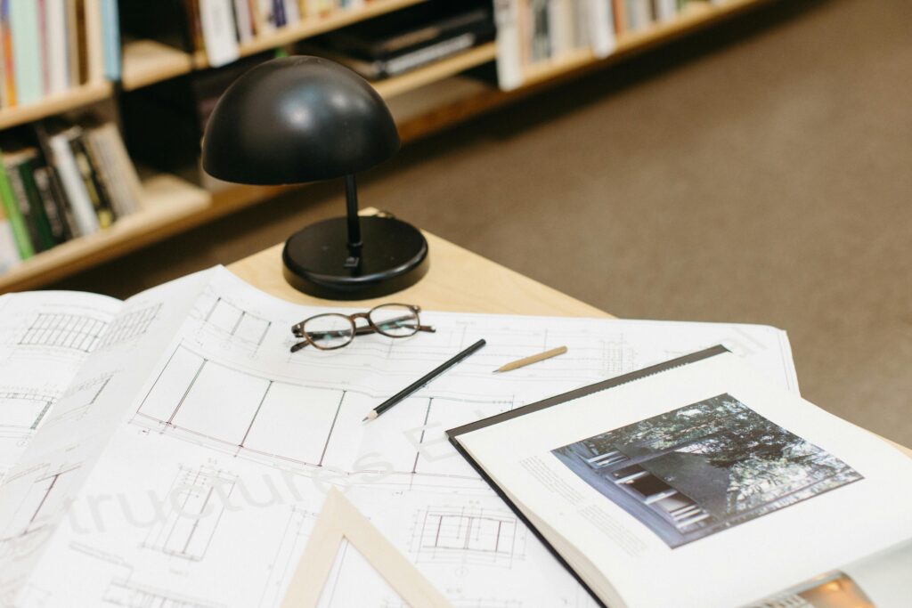 A workspace with architectural blueprints, glasses, and a desk lamp on display.