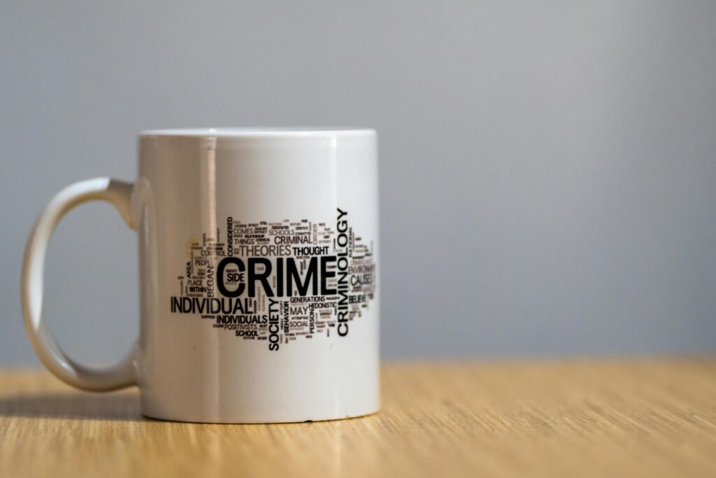White ceramic mug with criminology-themed word cloud design on wooden surface.