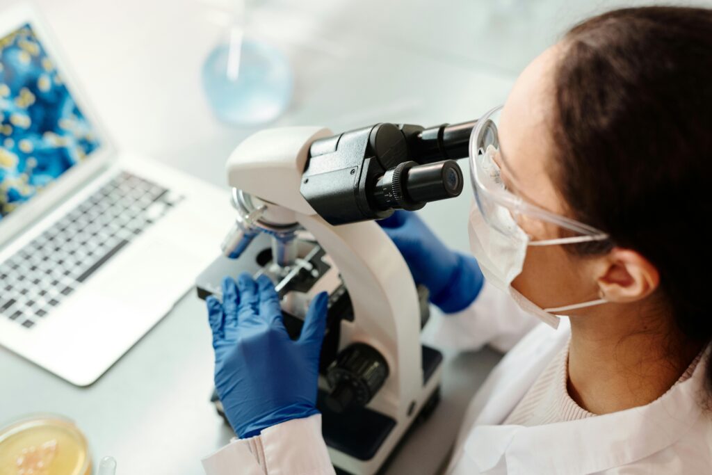 Scientist in protective gear examining samples with microscope in laboratory setting.